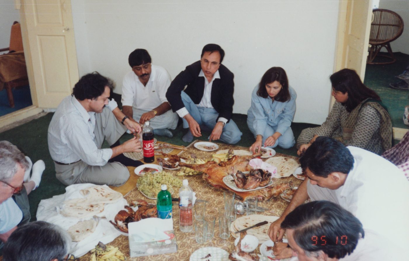 Dr. Abdulla and colleagues sitting on the floor around a lunch of barbecued goat and flatbread at the Afghanistan border, date-stamped October 1995