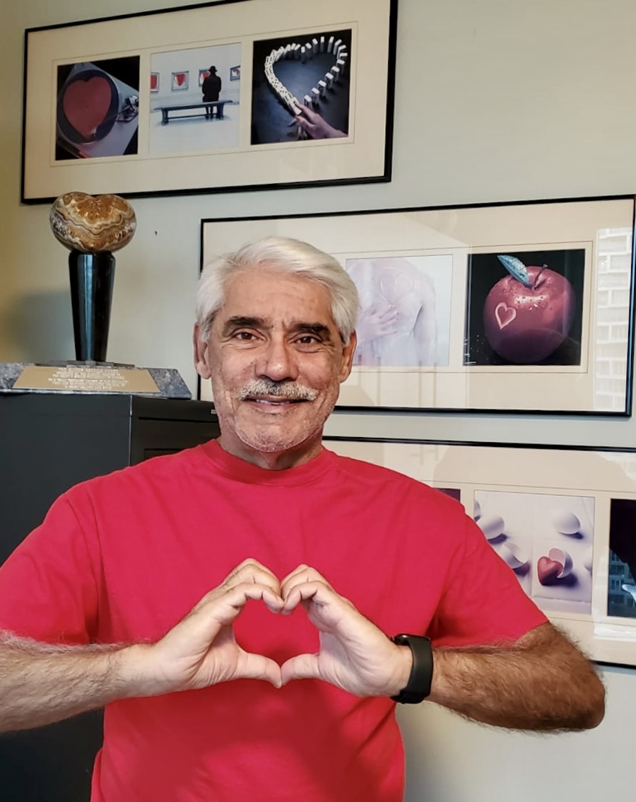 Dr. Abdulla making a heart shape with his hands, in front of his collection of heart-themed art, during Heart Health Month