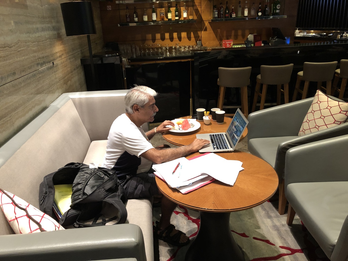 Dr. Abdulla working past midnight at a hotel lounge table in Singapore, reviewing medical reports on his laptop and in printed papers, 2019